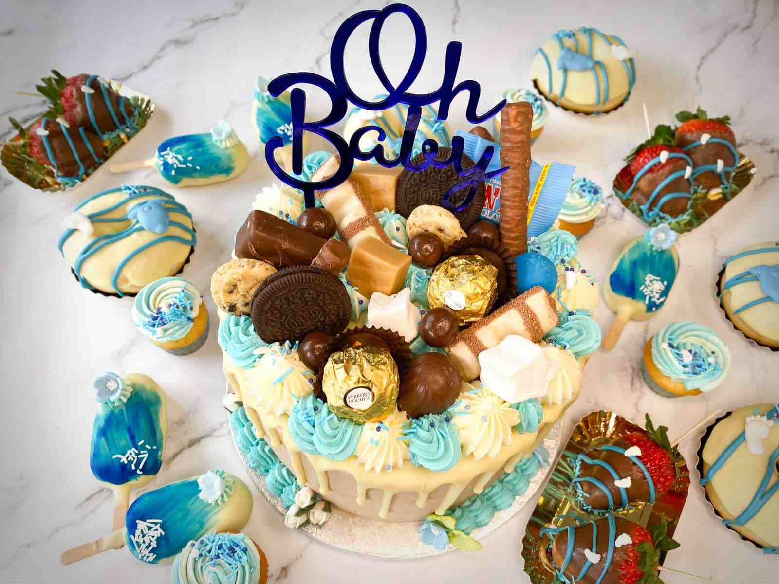 Babyshower sweet table in blauw met Oh Baby-driptaart, cakesicles, cupcakes en chocolade-aardbeien