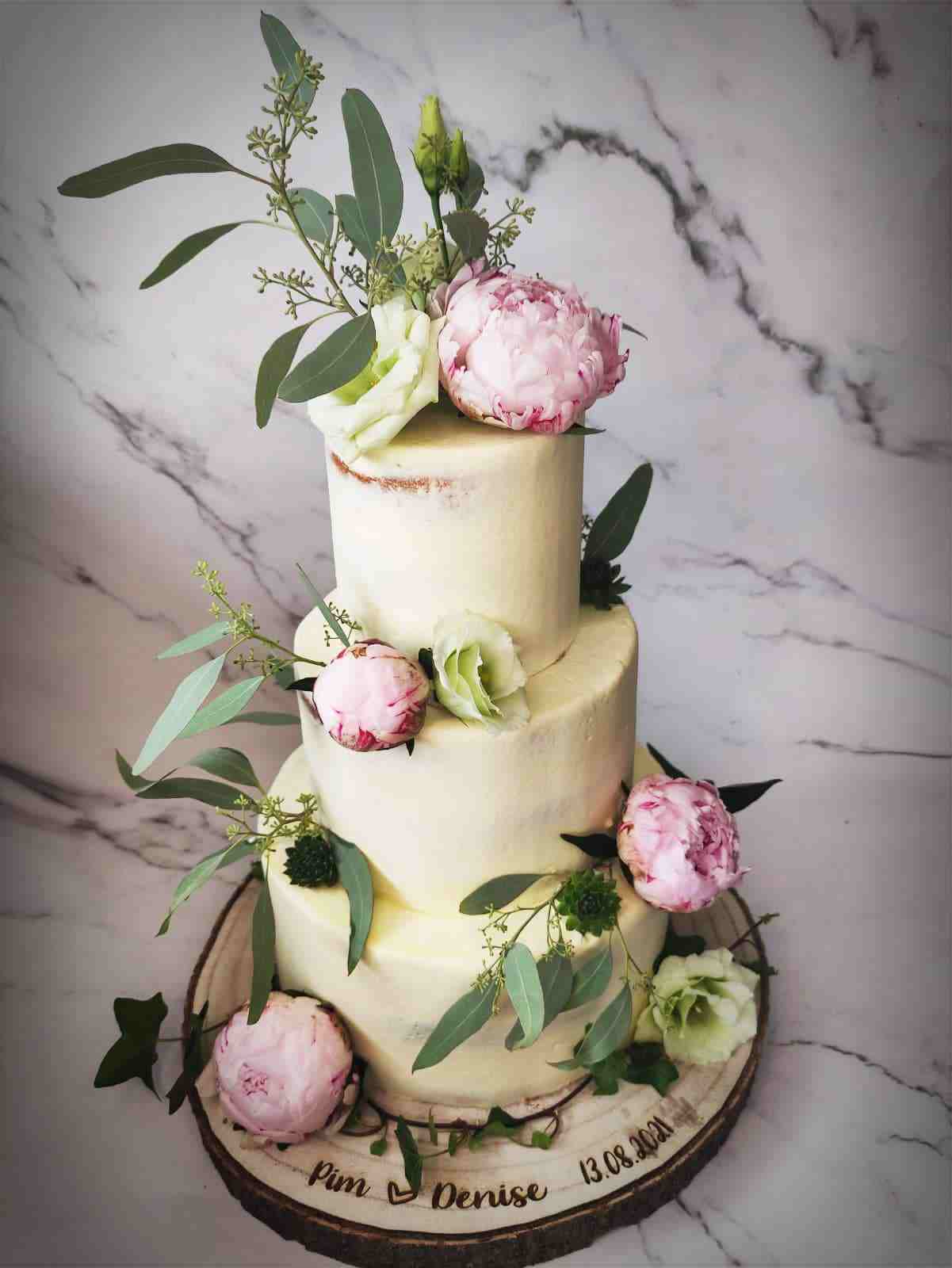 Drielaagse semi-naked bruidstaart met roze pioenrozen en eucalyptus op een houten boomschijf