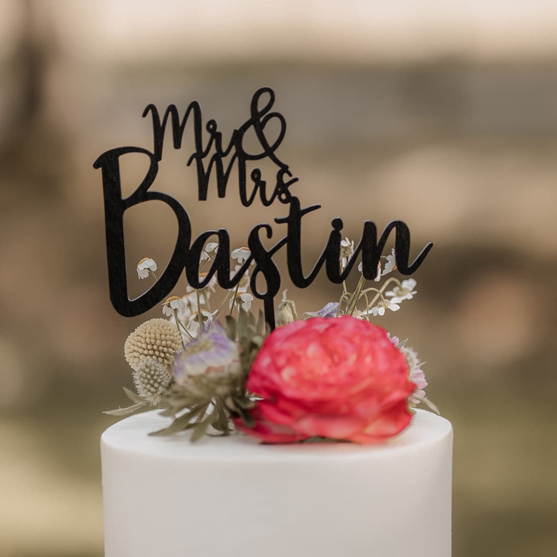 Witte bruidstaart met veldbloemen, rode ranonkel en zwarte Mr & Mrs-naamtopper