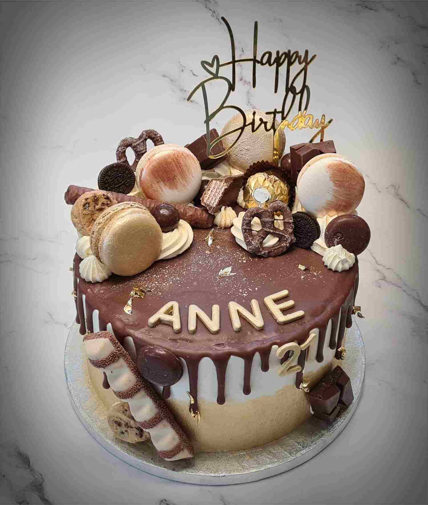 Chocolade drip cake met macarons, koekjes en bonbons, gouden letters Anne en het cijfer 21