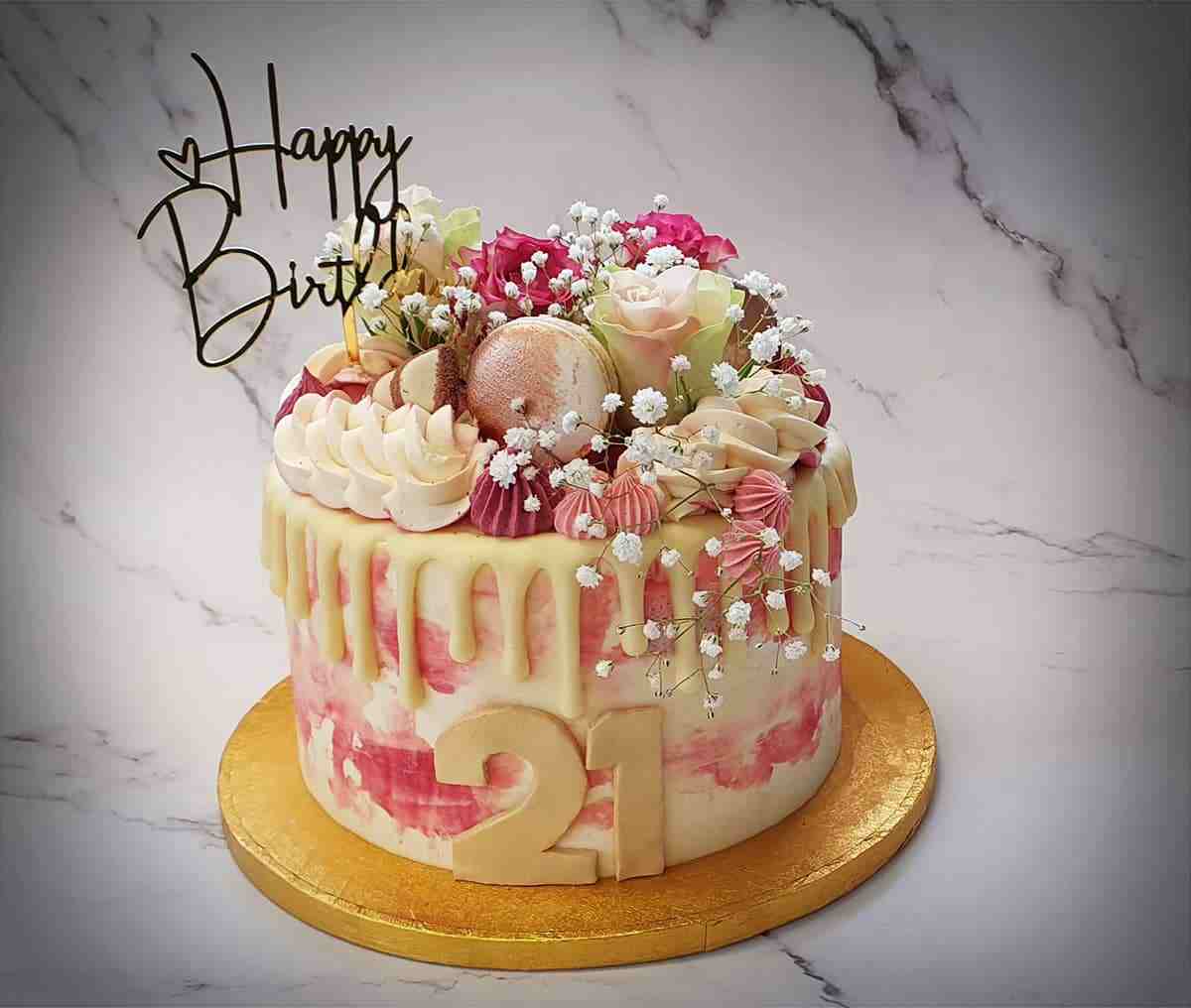 Roze driptaart voor een 21e verjaardag met verse bloemen, macarons en botercreme-toefjes