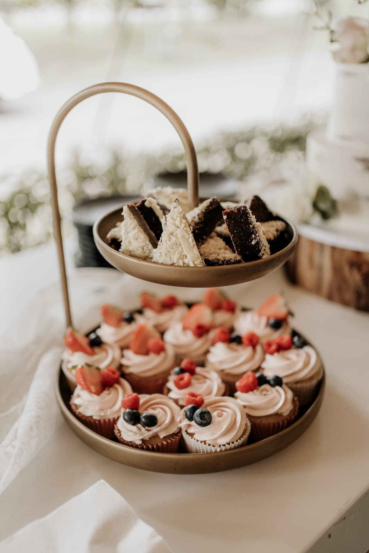Gouden etagère met brownies en cupcakes met aardbeien en blauwe bessen op een bruiloft