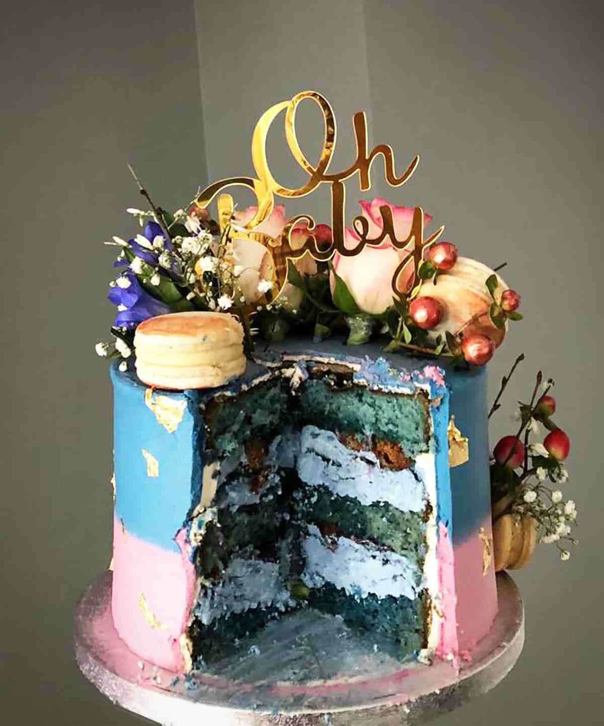 Aangesneden gender reveal taart met blauwe lagen, verse bloemen en gouden Oh Baby-topper