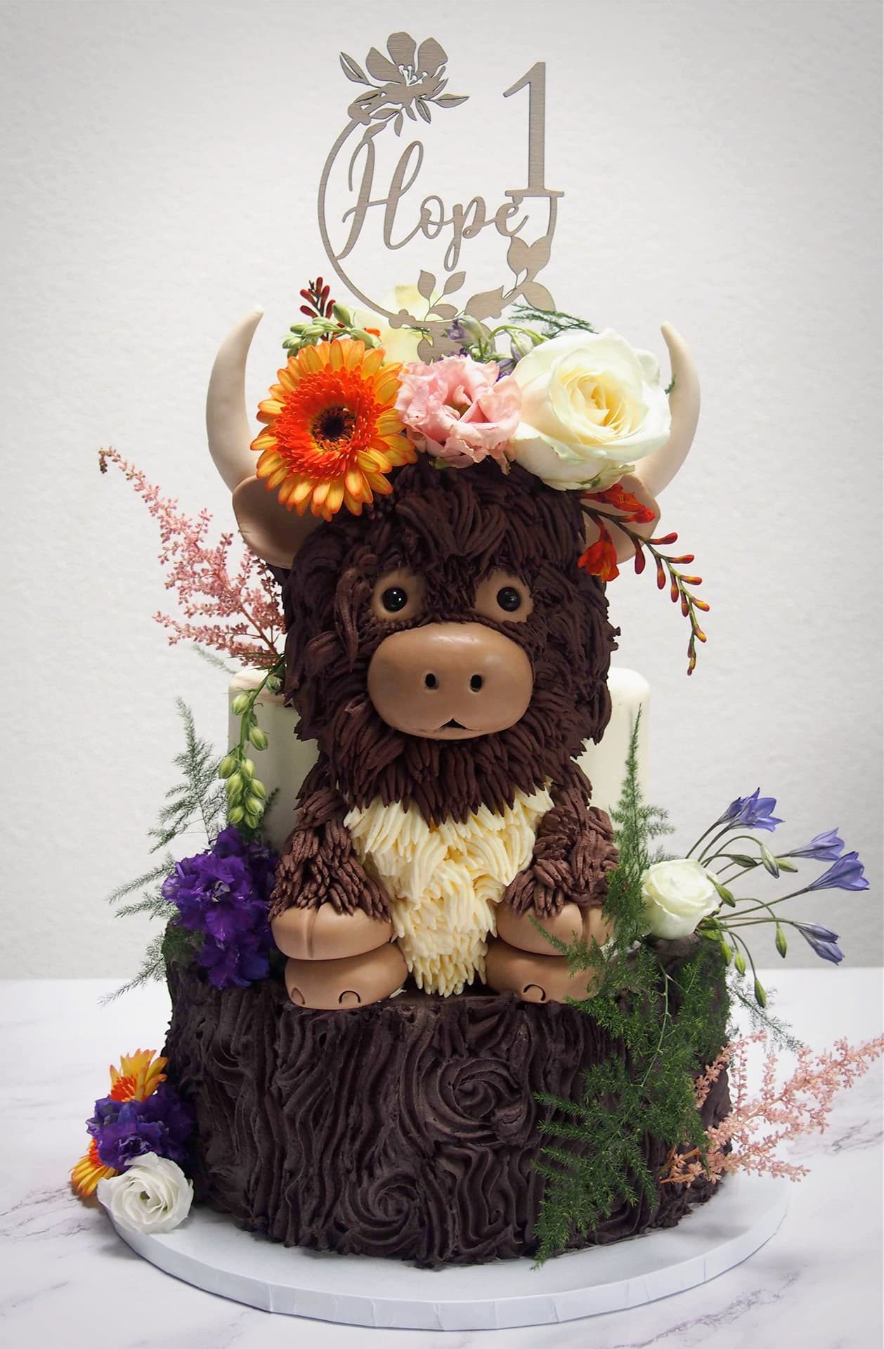 Verjaardagstaart in de vorm van een Schotse hooglander met verse bloemen en houten cijfertopper