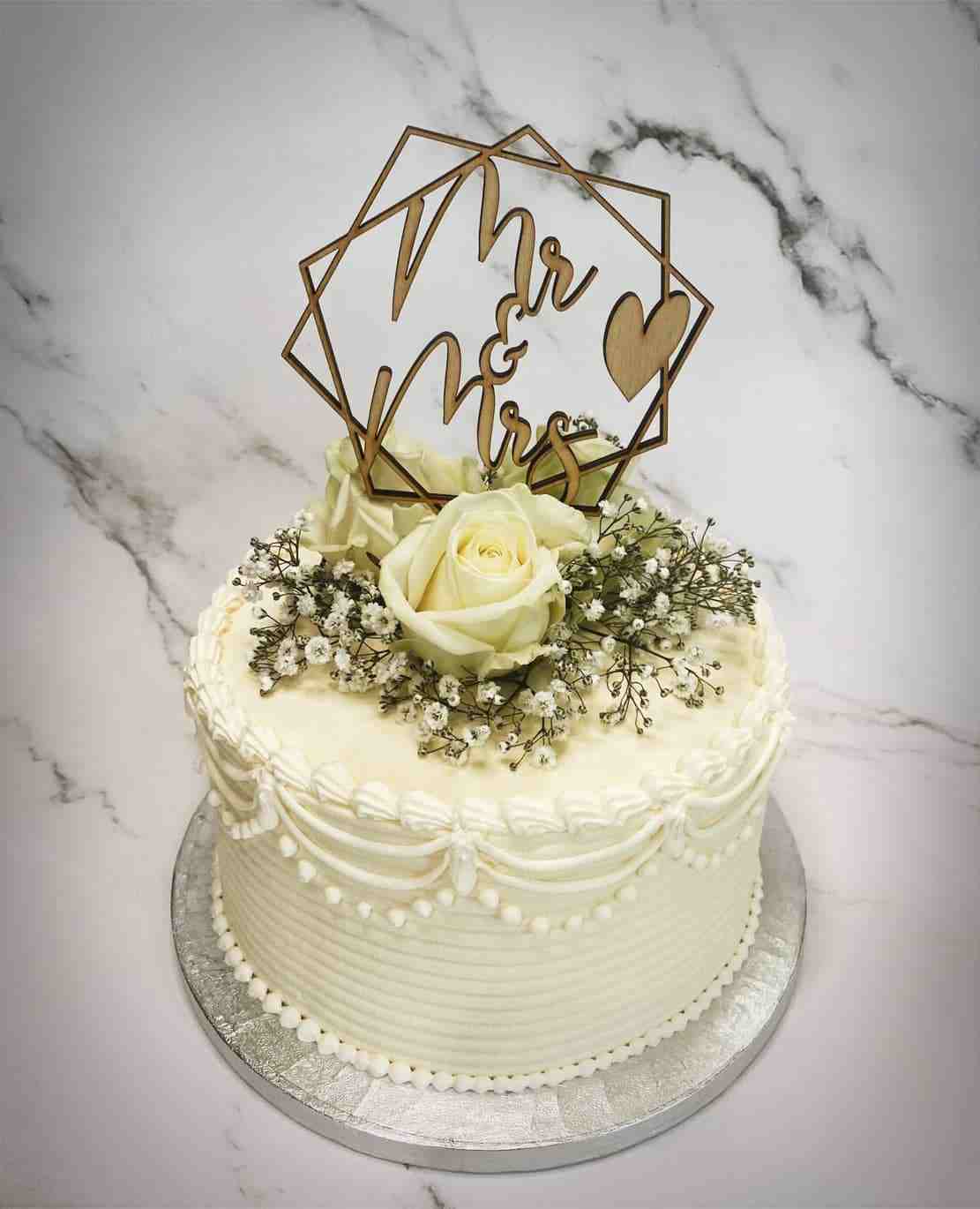 Klassieke witte bruidstaart met sierlijke botercreme, rozen, gipskruid en houten Mr & Mrs-topper
