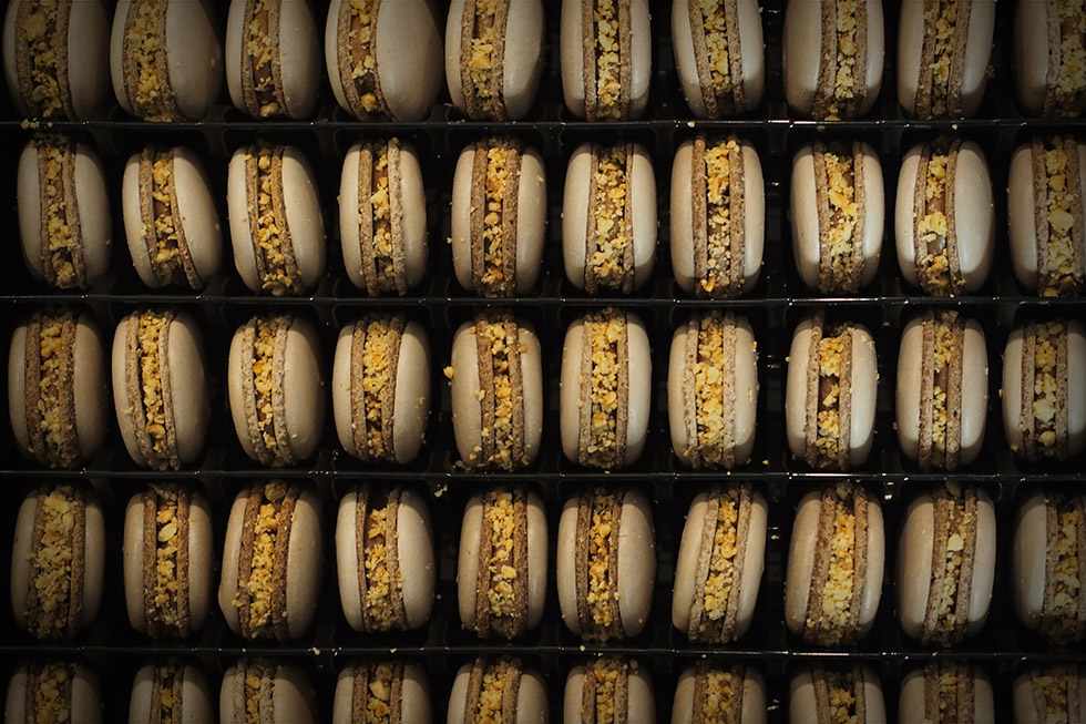 Rijen ambachtelijke macarons gevuld met crème en krokante notencrunch