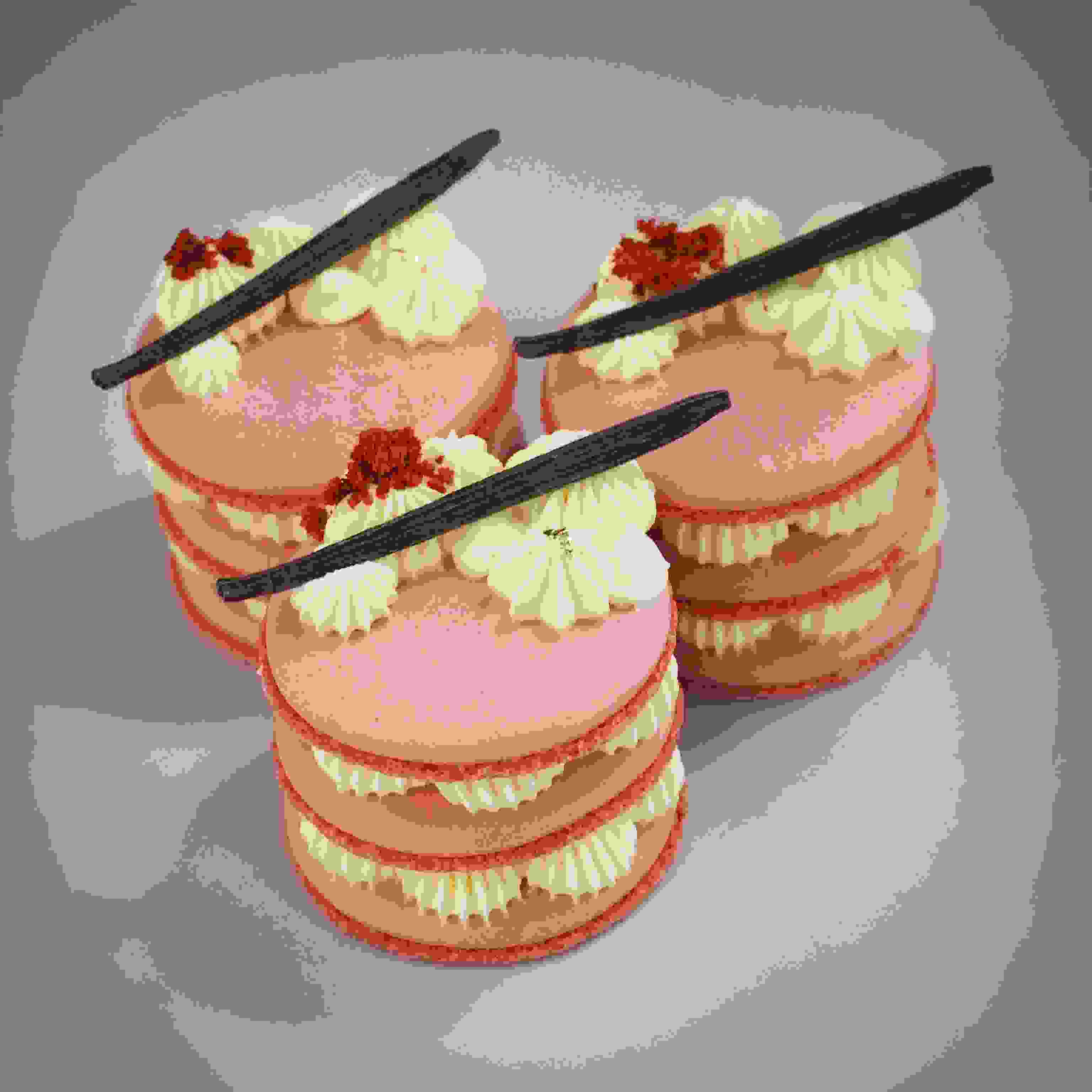 Drie gestapelde macarontaartjes met crèmetoefjes, rood fruitcrunch en vanillestokjes