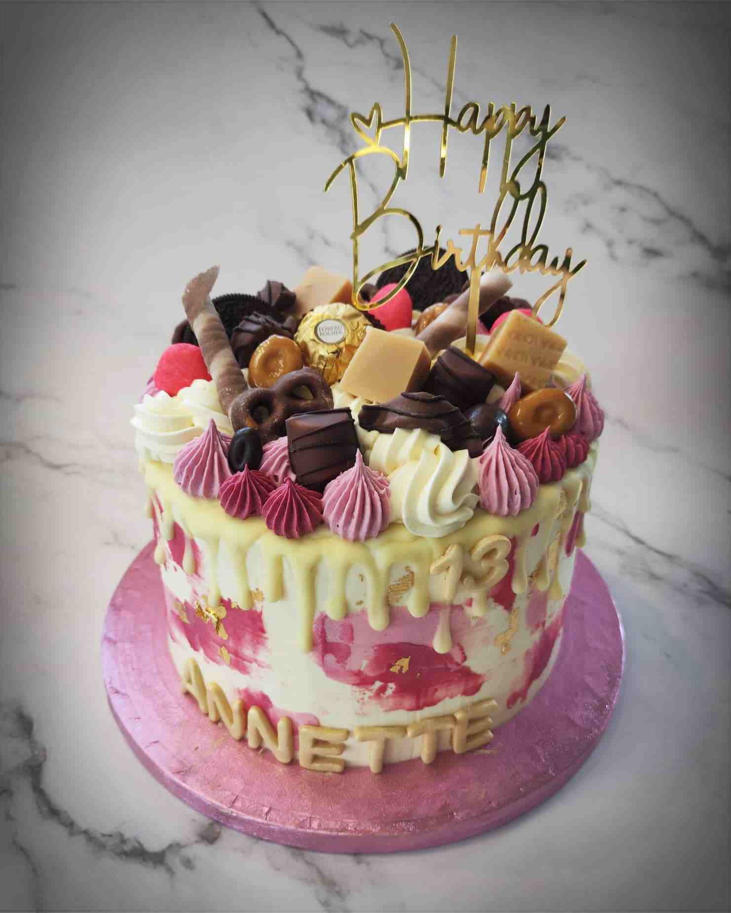 Roze-witte driptaart vol snoep en chocolade met gouden Happy Birthday-topper voor Annette (13)